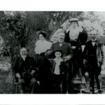 An old black and white image of a family posing in front of a large oak tree.