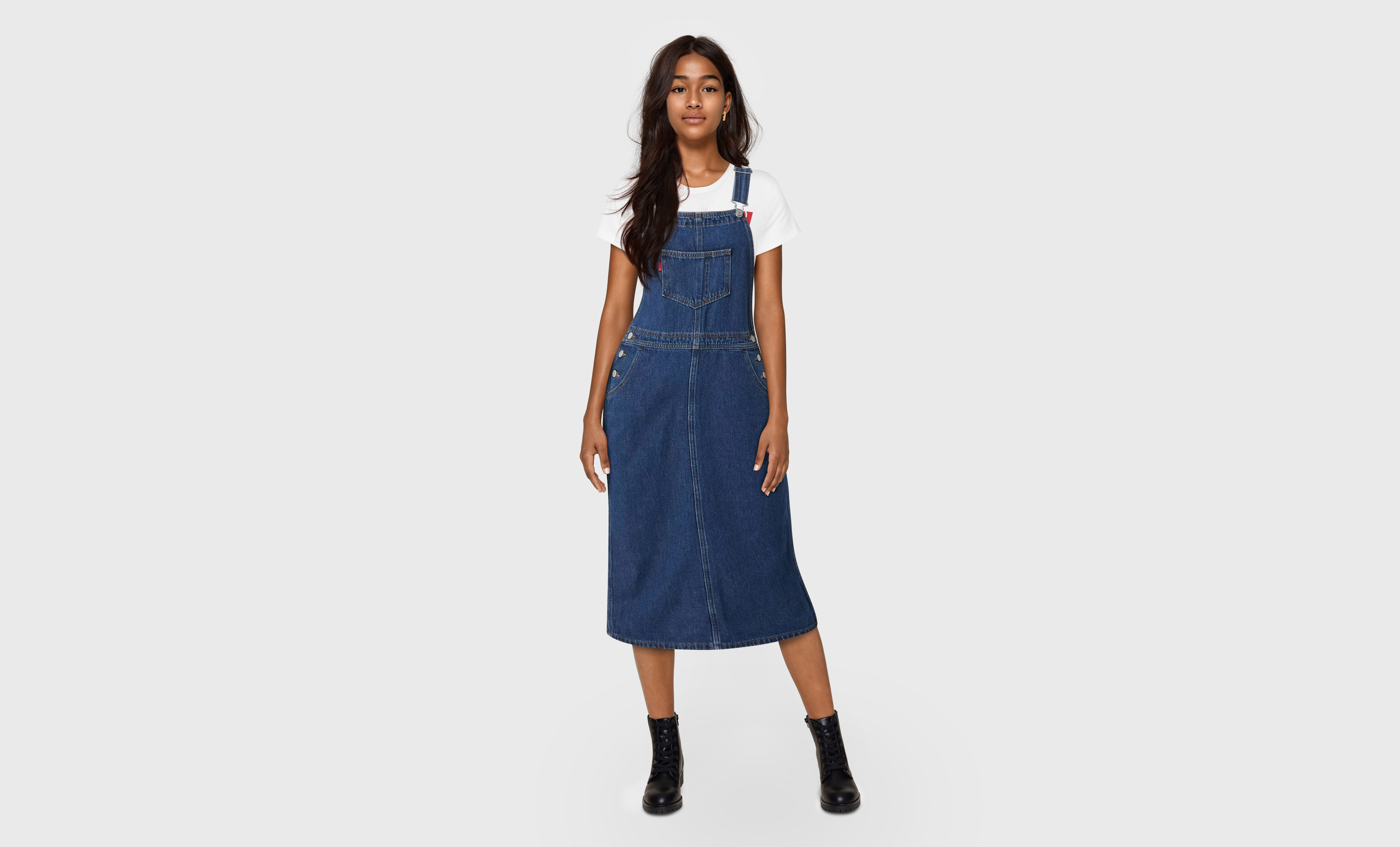 An AI-generated model with long brown hair stands in front of a plain grey background wearing a Levi's® denim dress over a white T-shirt.