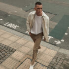 A person walking on the sidewalk looking over their shoulder. They have a hand in their pocket and are wearing a beige Dockers® button up over a white T-shirt and tan Dockers® GO pants.