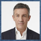 A headshot of Gianluca Flore on a blue denim textured background.