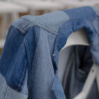 A patchwork denim jacket drapes on the back of a white chair