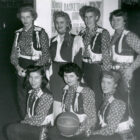 A black and white image of seven Texas Cowgirls basketball players, four standing, three kneeling in the front. The woman in the front center holds a basketball.