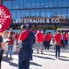 LS&Co. employee volunteers gather around the front of the LS&Co. San Francisco headquarters wearing red volunteer shirts. A red logo in the top left corner reads "Community Day 25 Years"