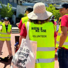 the back of an employee wearing a sun hat and a neon safety vest holding a canvas tote bag.