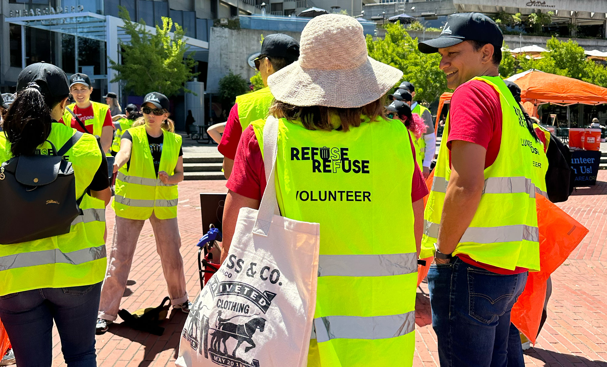 the back of an employee wearing a sun hat and a neon safety vest holding a canvas tote bag.