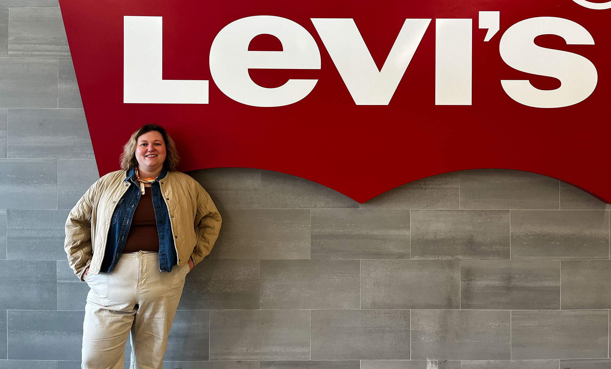 Levi's manager Kelly Perl smiles and stands in front of a wall featuring a large red Levi's batwing logo.