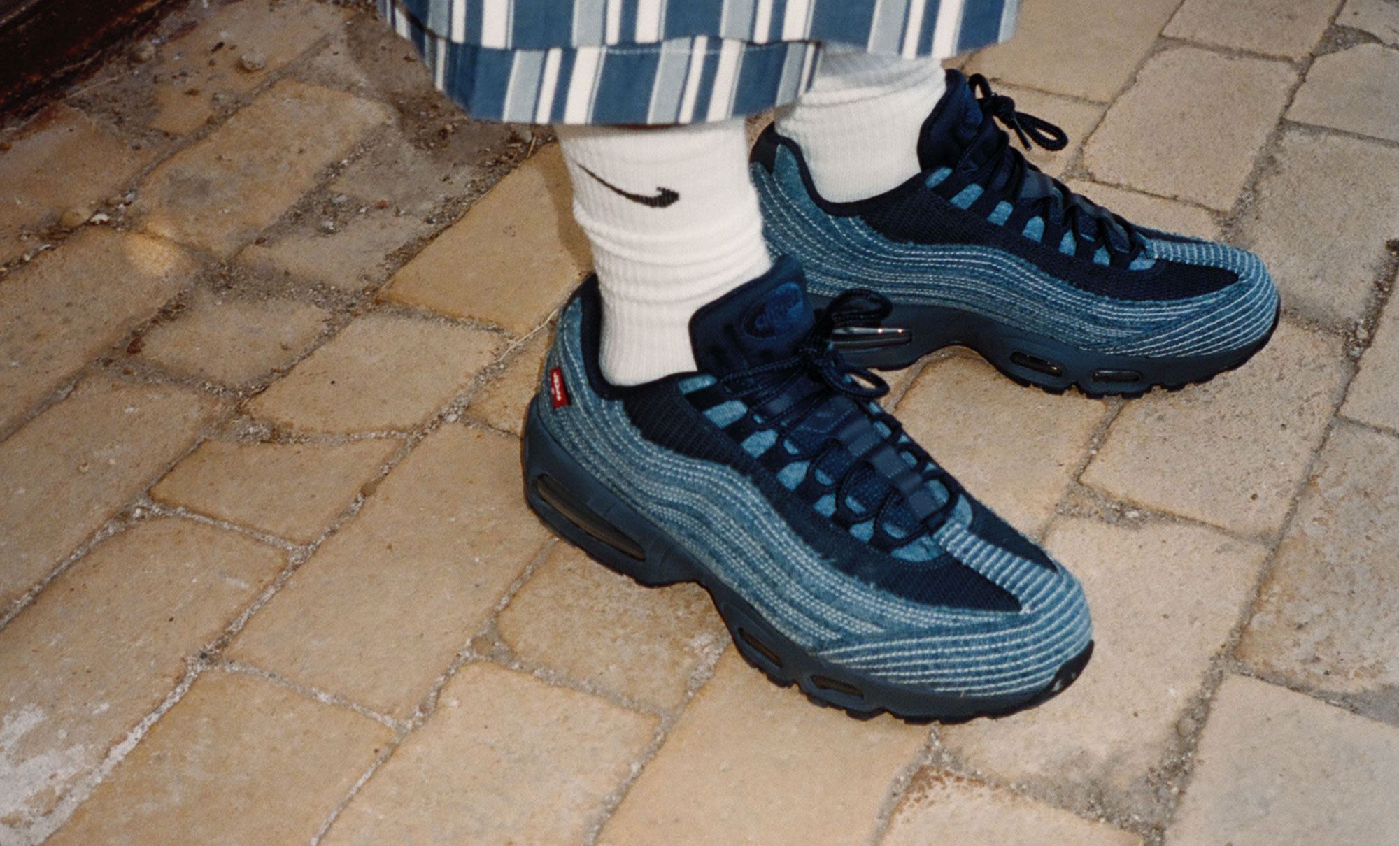 A pair of feet wearing a Levi's® x Nike Air Max 95 in blue denim with white Nike socks.