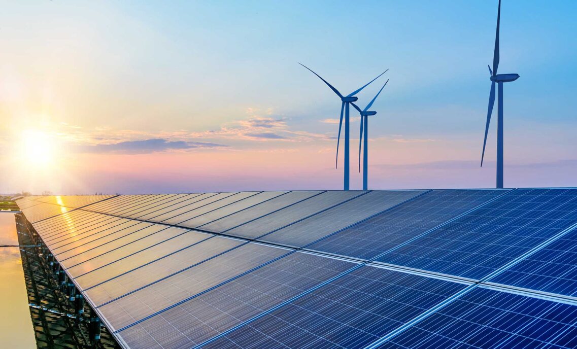 A solar paneled roof and three windmills against a sunset sky