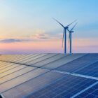 A solar paneled roof and three windmills against a sunset sky