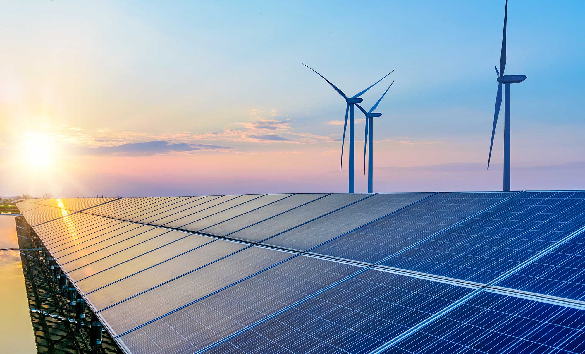 A solar paneled roof and three windmills against a sunset sky