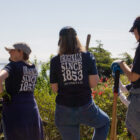 Three Levi Strauss & Co. employee volunteers stand with their backs to the camera facing an overlook of the San Francisco Bay Bridge. They hold gardening tools and wear baseball caps, Levi's® jeans and blue shirts that read "Originals Since 1853 Levi Strauss & Co."